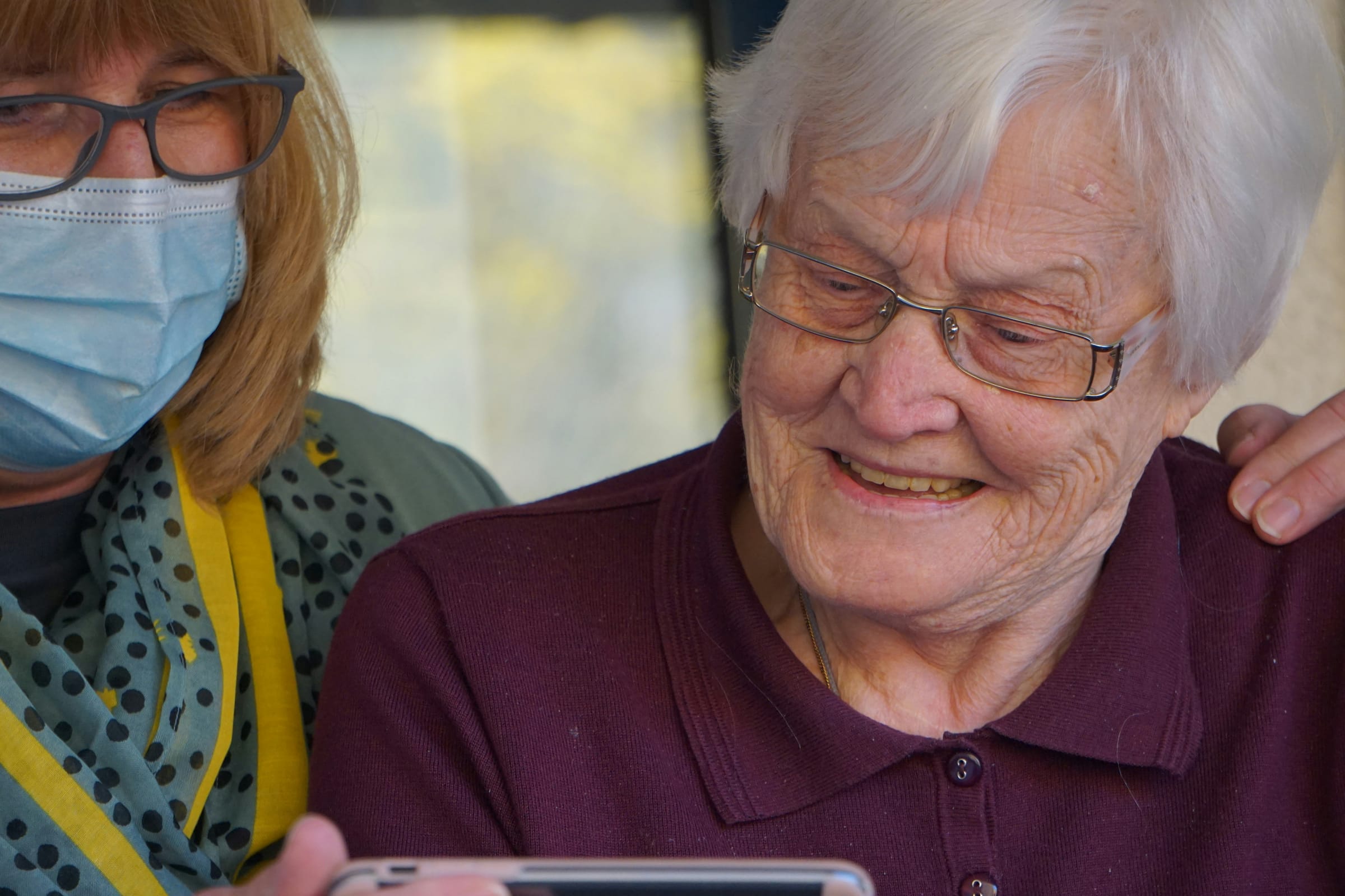 A carer and an older woman looking together at a phone screen