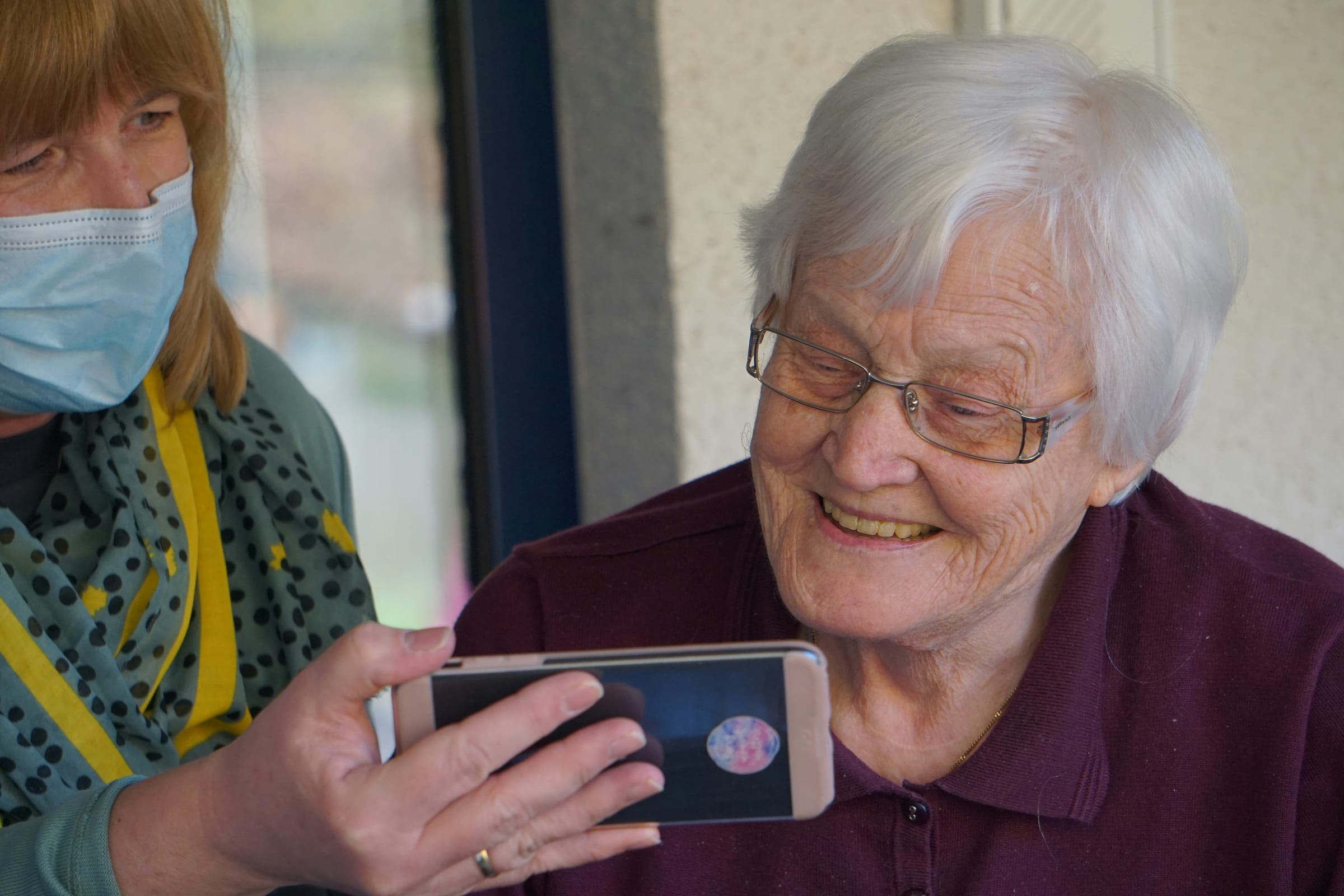 A carer showing a photo on a phone to a smiling older woman