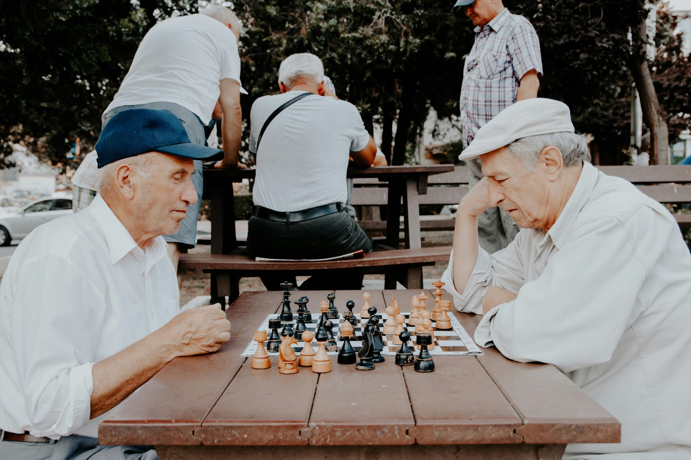 Older men playing chess at a park table on a summer evening