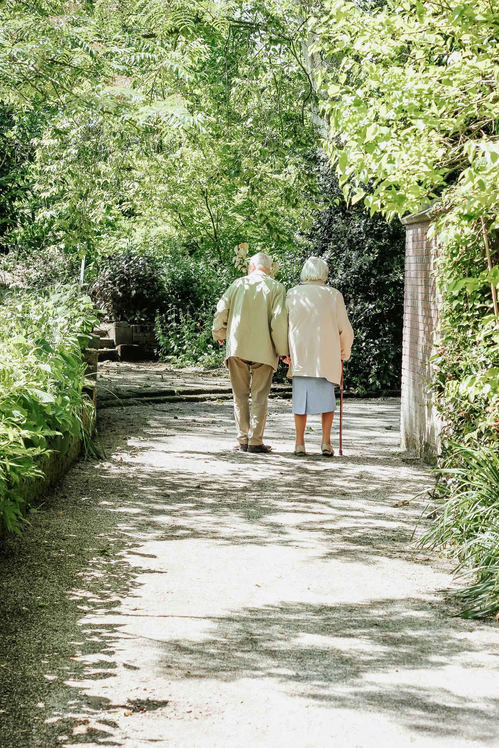 An older couple walking arm in arm along a garden path
