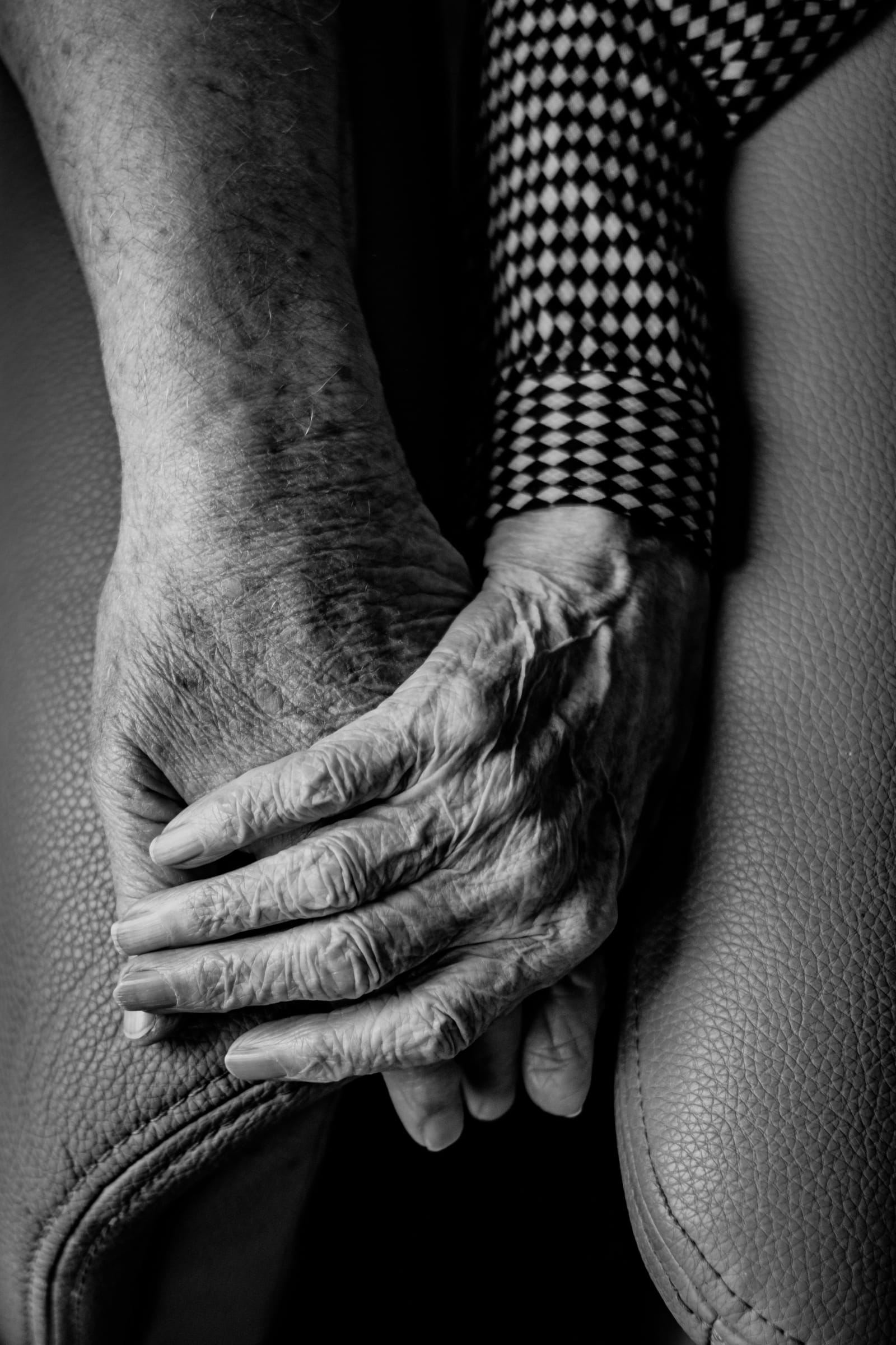 Two older hands resting one over the other on the arm of a chair