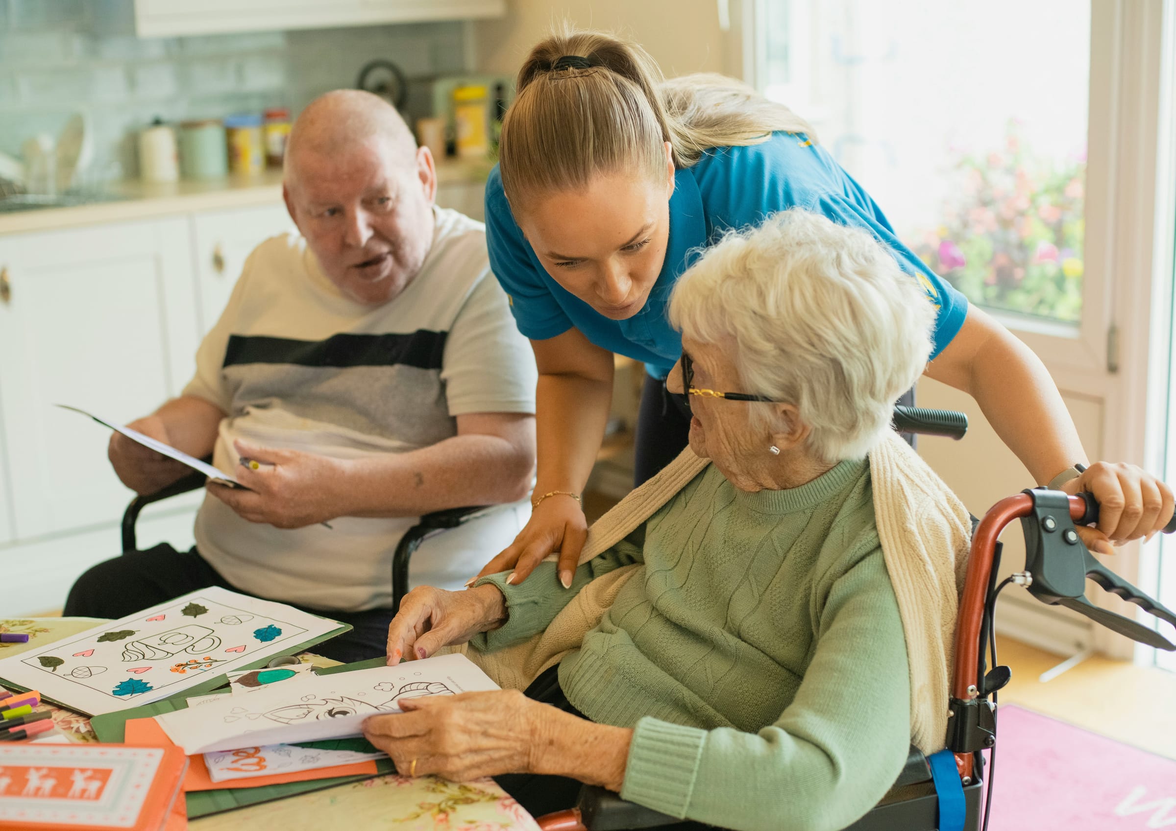 A carer working at the kitchen table with two clients
