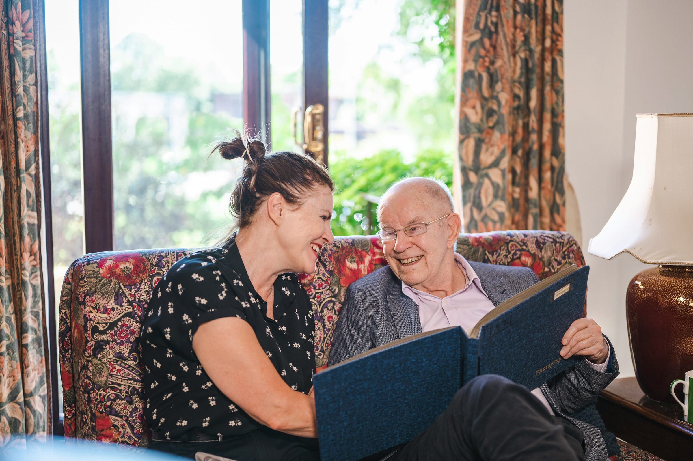 A carer and an older man laughing together over an old photo album